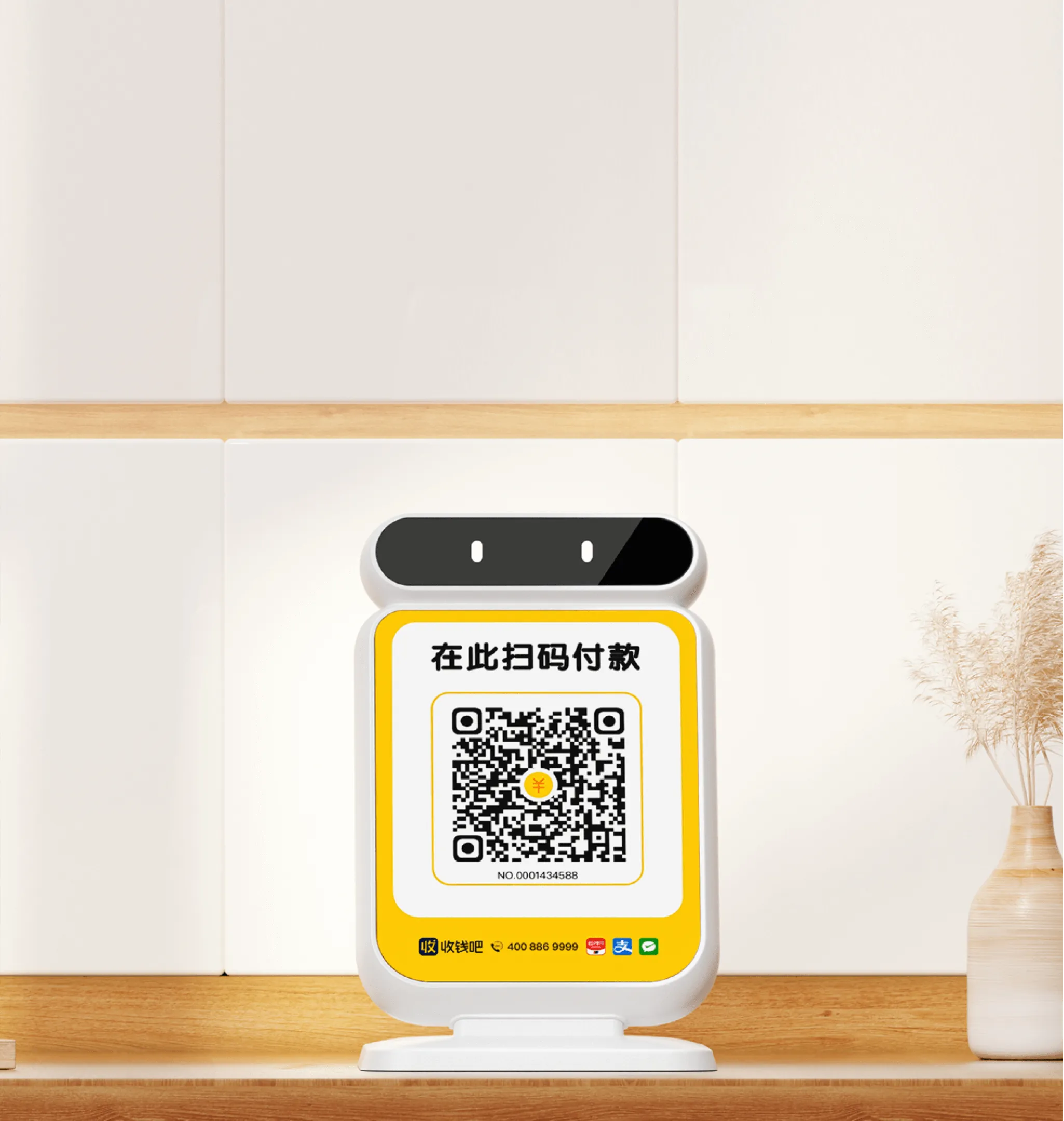 收钱吧收款码牌立在木质柜台上，正面展示扫码收款面板和稳固底座
